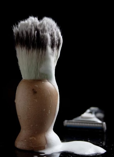Schaum auf Rasierpinsel, daneben eine Rasierklinge